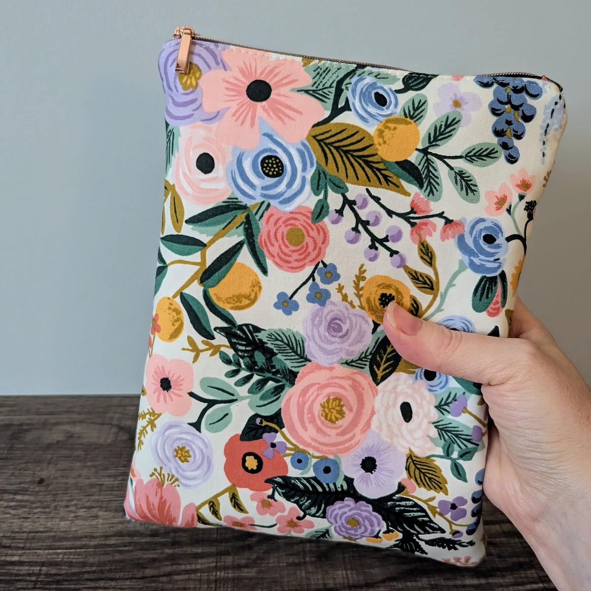 Floral-patterned pouch held by a hand against a neutral background