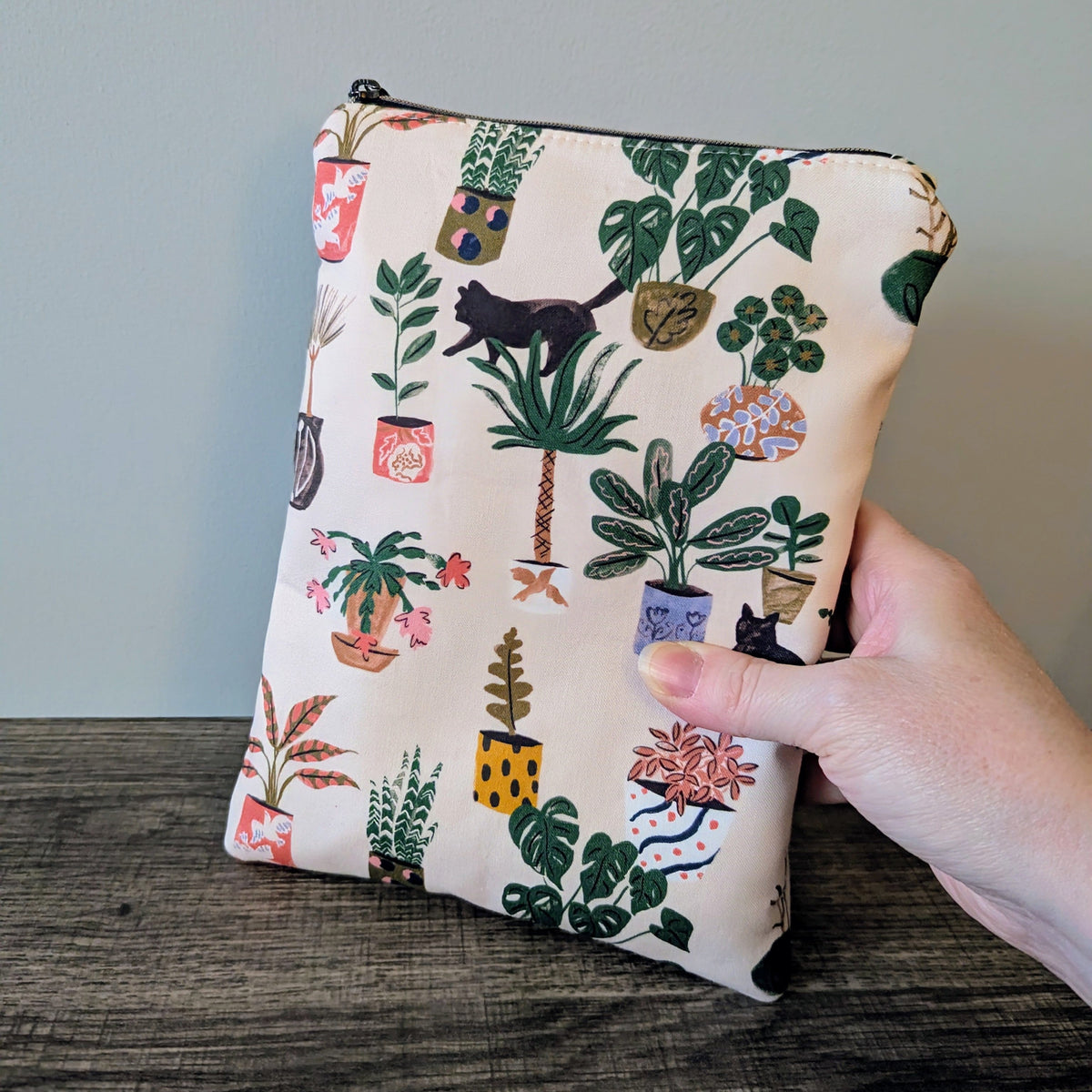 Pouch with plant and cat pattern held by a hand on a wooden surface