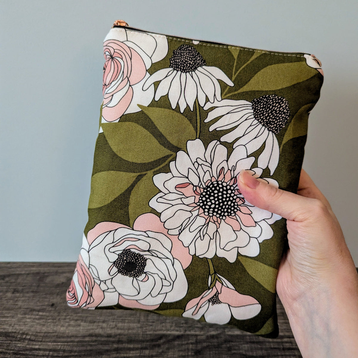 Floral-patterned pouch held by a hand against a neutral background