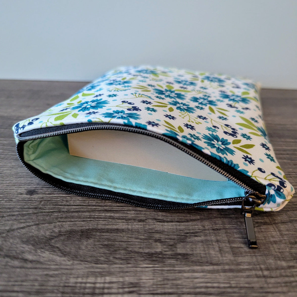 Floral-patterned pouch with a light blue interior on a wooden surface