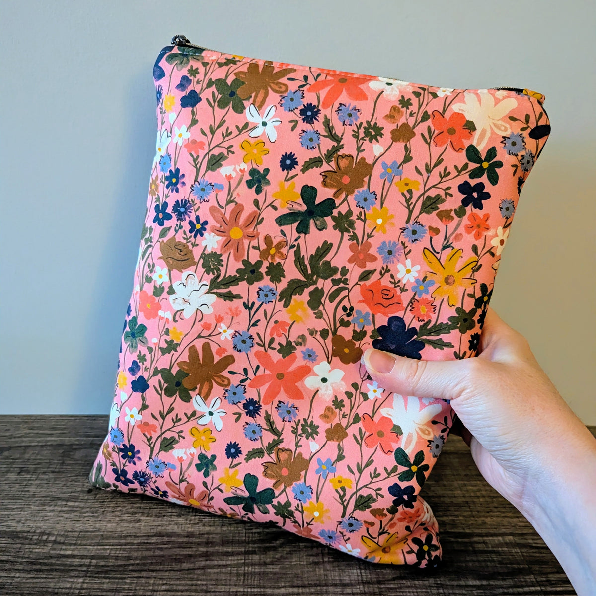 Floral-patterned bag held by a hand against a neutral background