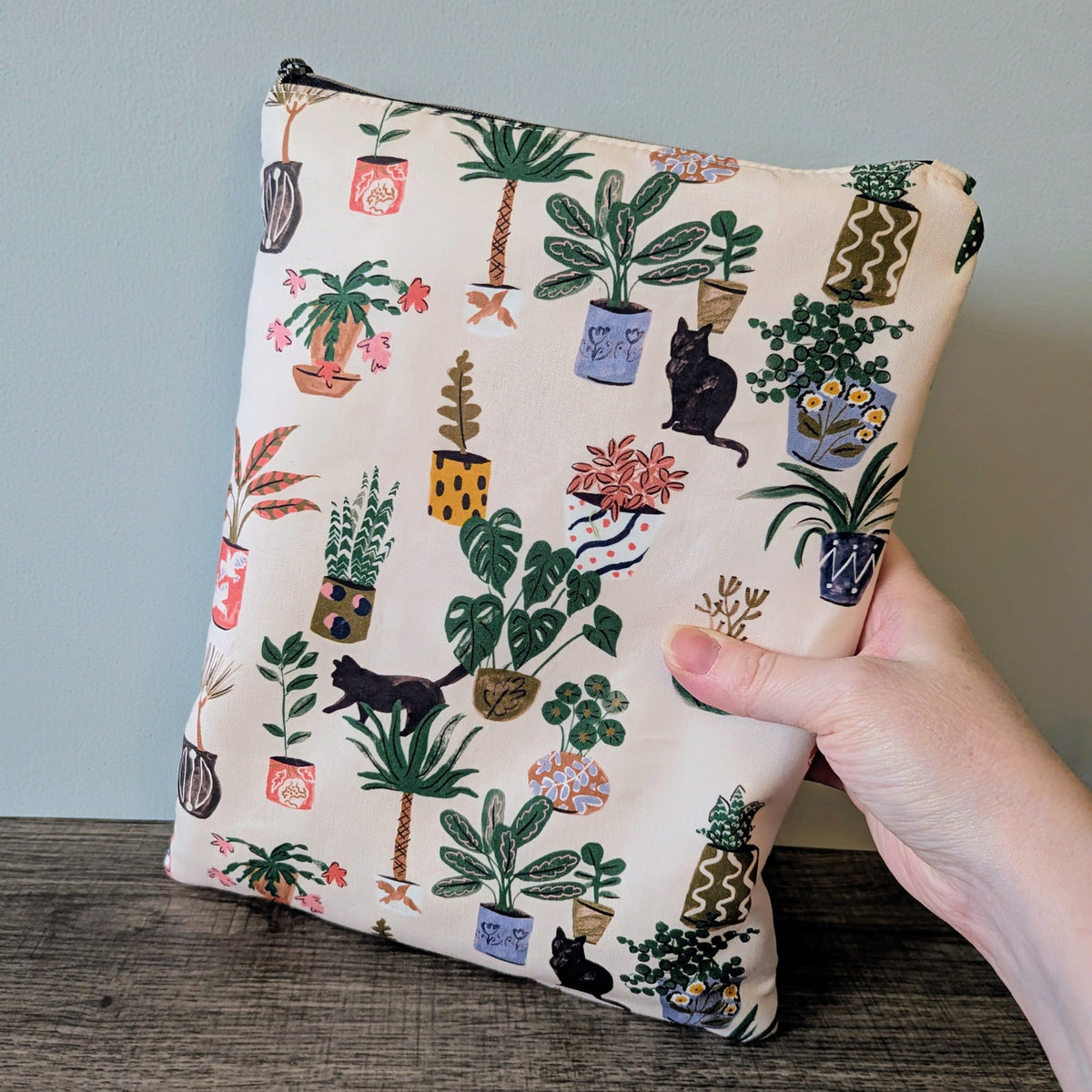 Pouch with plant and cat pattern held by a hand against a gray background