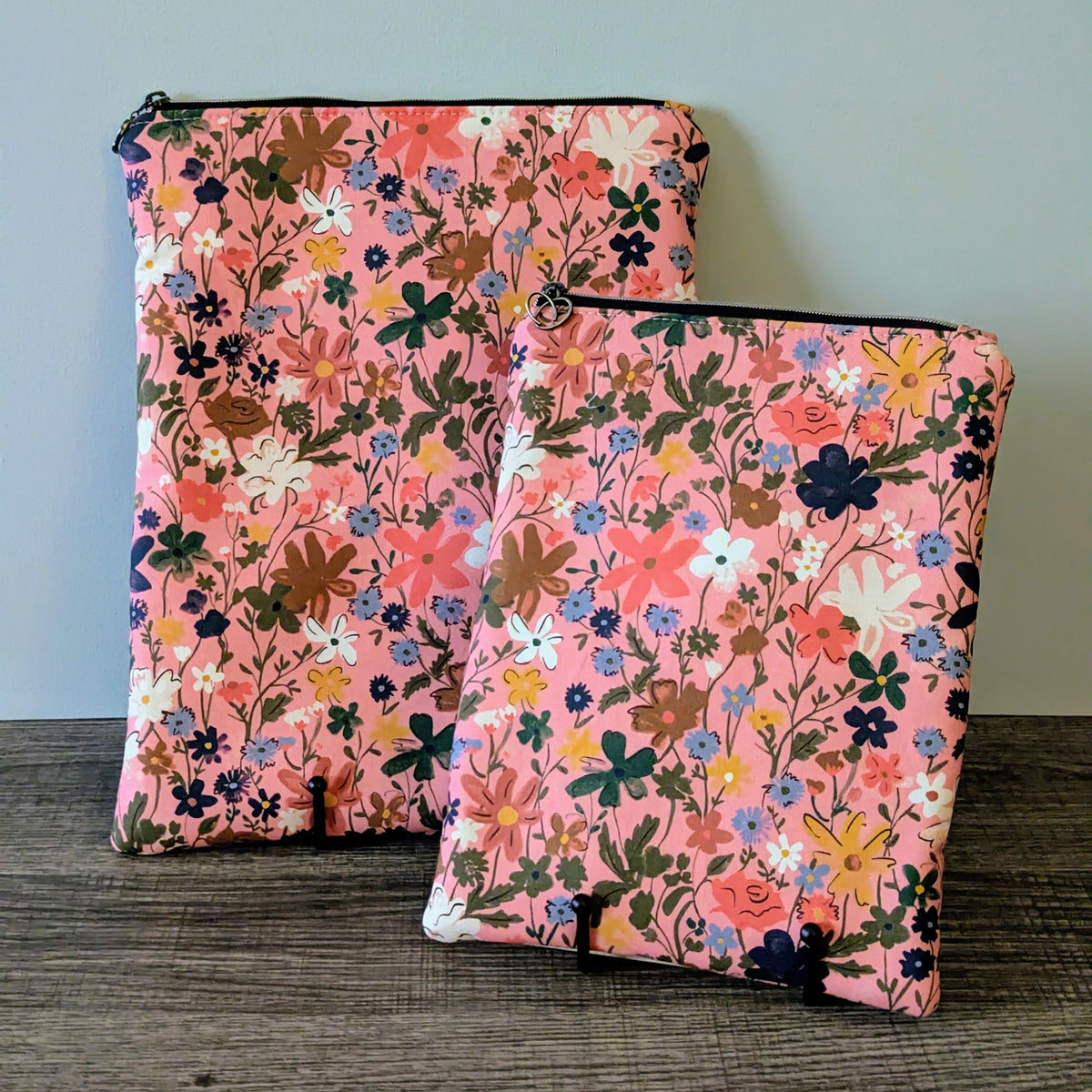 Two pink floral-patterned bags on a wooden surface with a light gray background