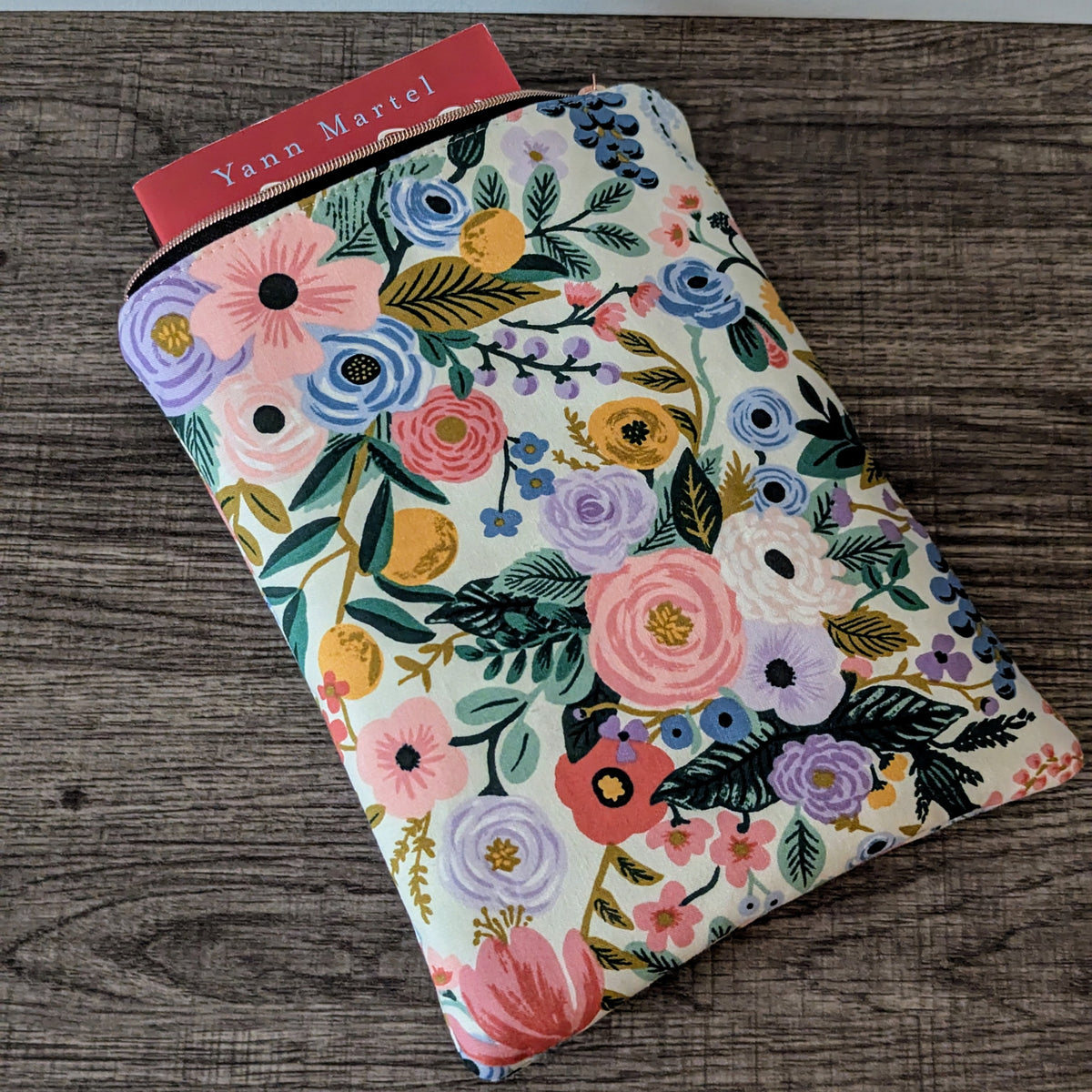 Floral-patterned pouch on a wooden surface with a visible brand label.