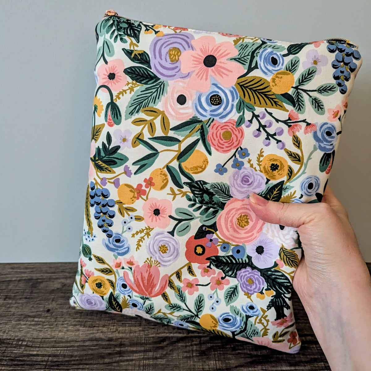 Floral-patterned pillow held by a hand against a neutral background