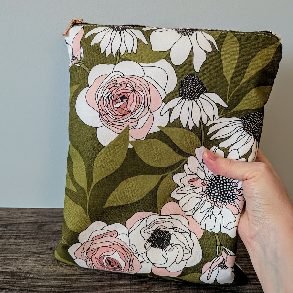 Floral-patterned cushion held by a hand on a wooden surface with a neutral background
