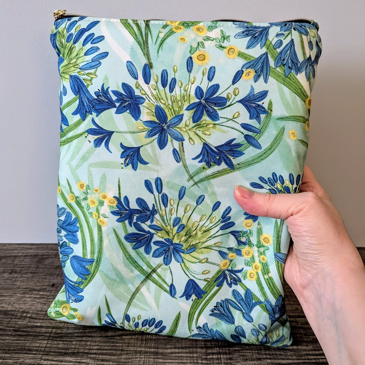 Floral-patterned pouch held by a hand on a wooden surface with a neutral background