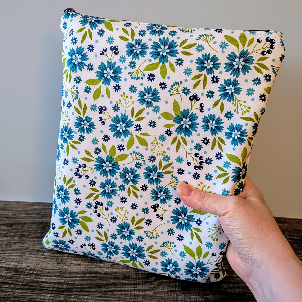 Floral-patterned bag held by a hand on a wooden surface with a neutral background