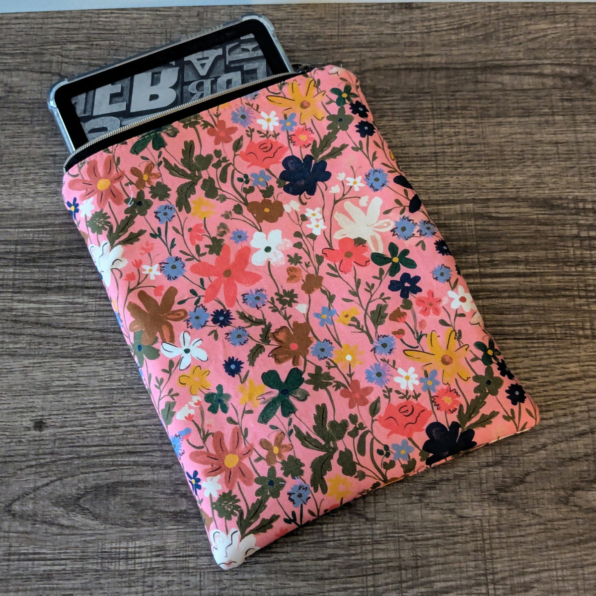 Floral-patterned notebook on a wooden surface with a black and white object in the background.