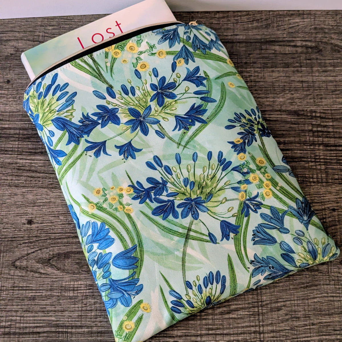 Floral-patterned pouch on a wooden surface with a book titled 'Lost' in the background.