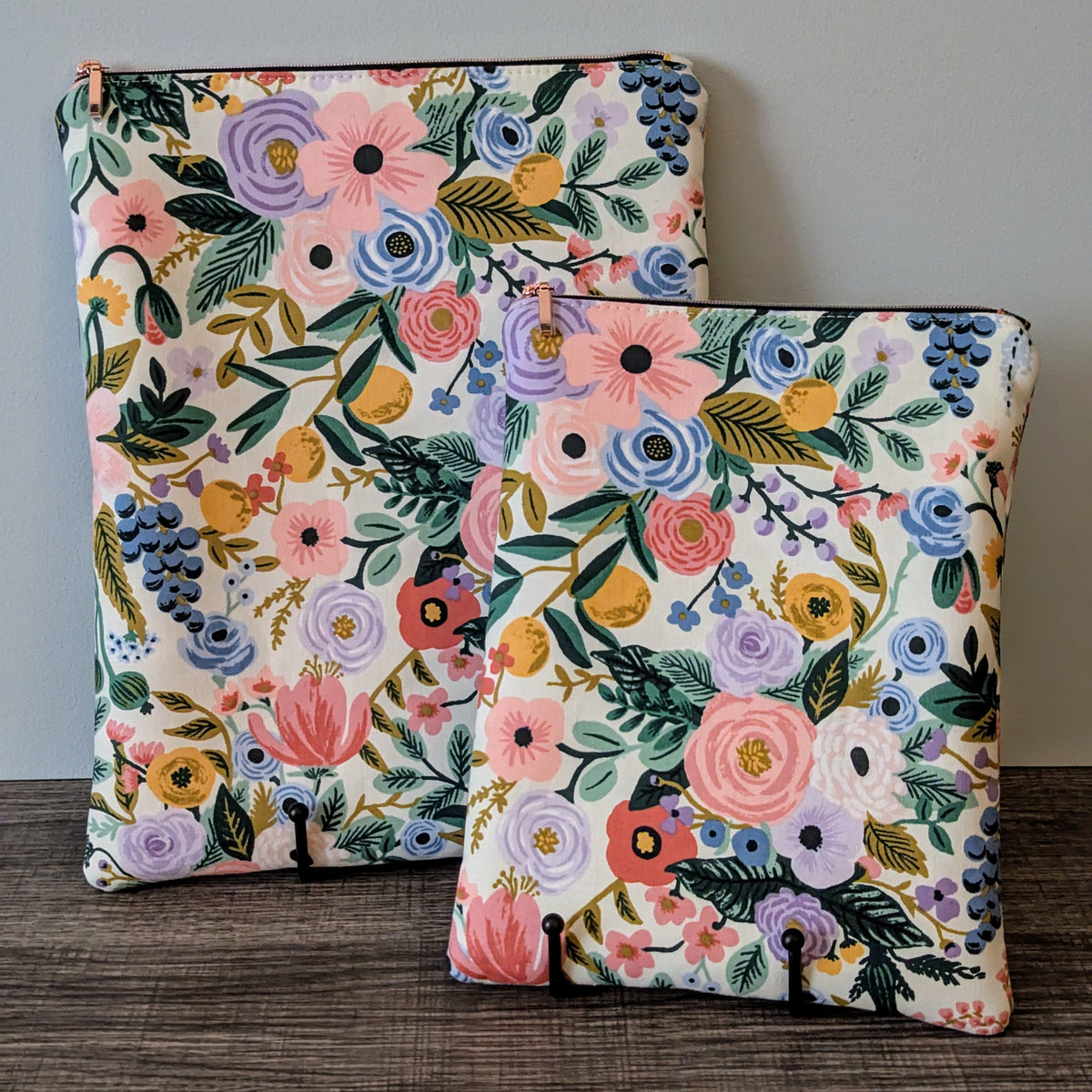 Two floral-patterned pouches on a wooden surface with a gray background