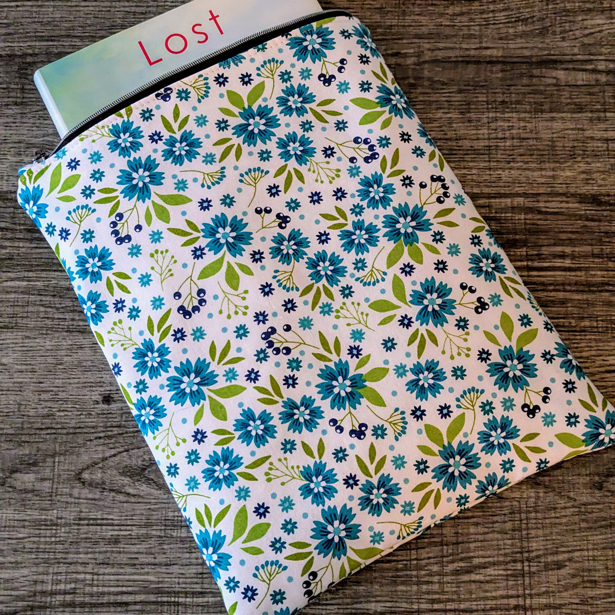 Floral-patterned notebook on a wooden surface with a book titled 'Lost' partially visible.