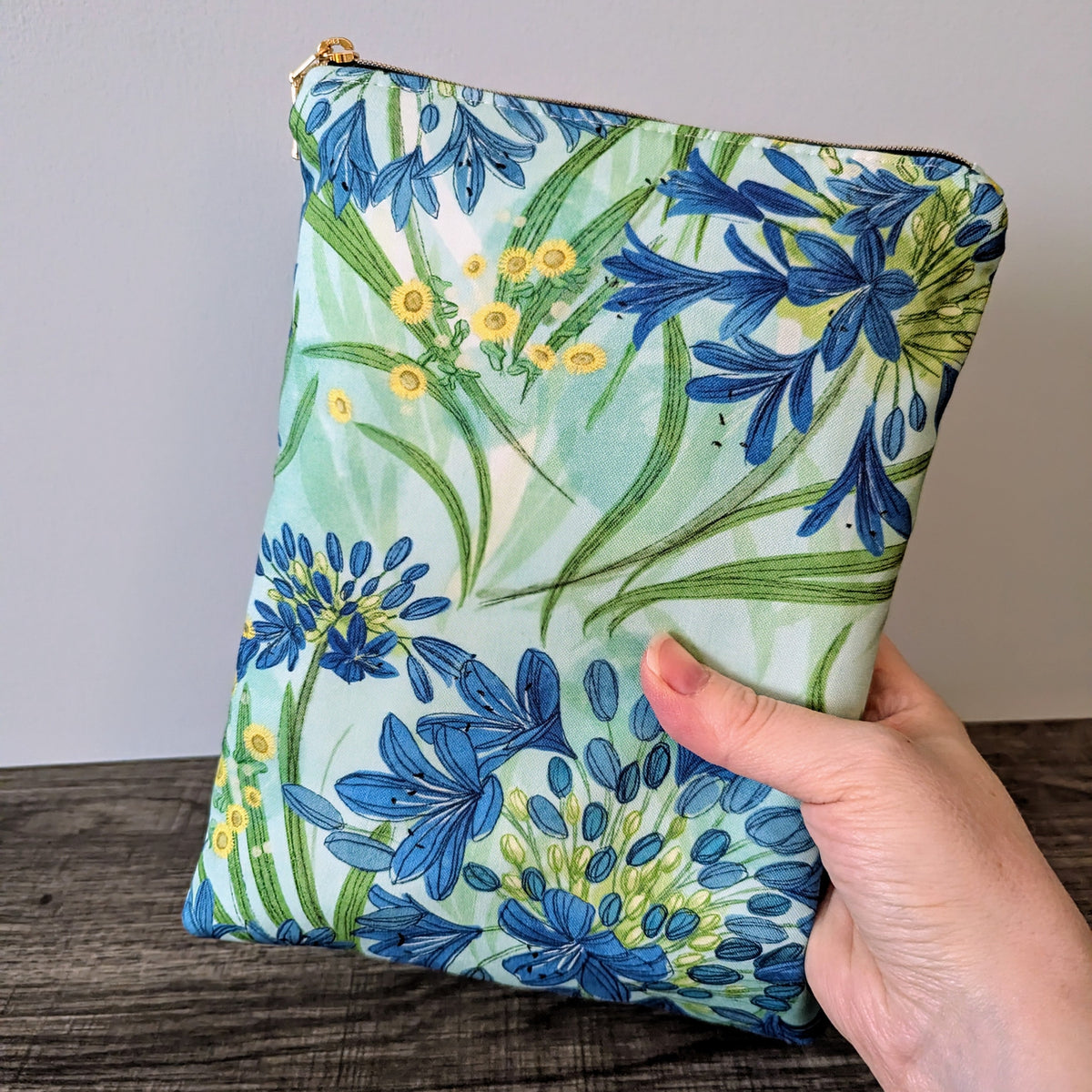 Floral-patterned pouch held by a hand on a wooden surface with a gray background